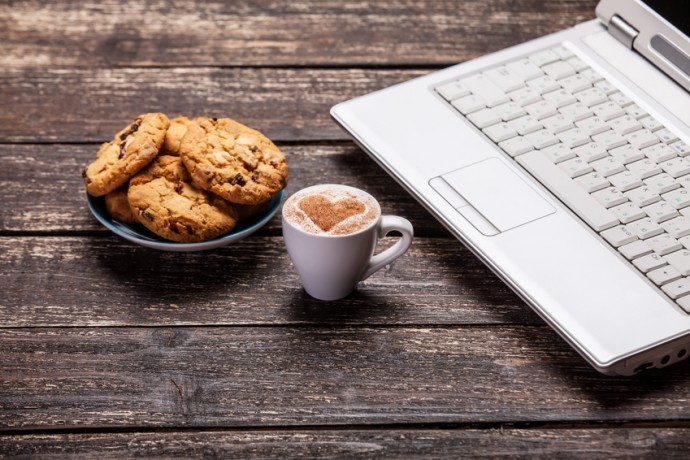 cookie and cup of coffee with laptop on wooden table.